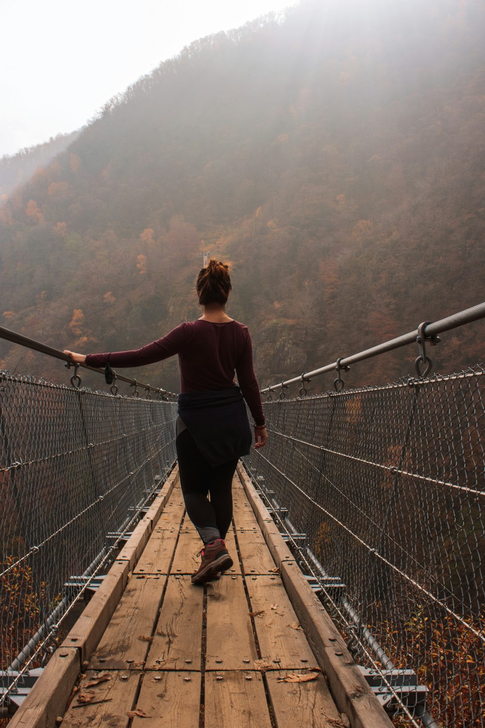 woman in black long sleeve shirt and black pants walking on brown wooden bridge during daytime