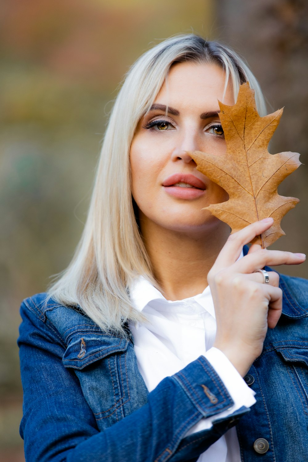 woman in blue denim jacket holding brown maple leaf