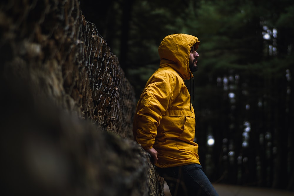 man in yellow hoodie leaning on brown wooden fence during daytime