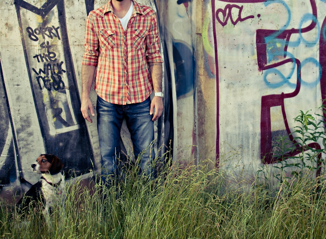 man in orange and white plaid button up shirt standing beside wall with graffiti during daytime