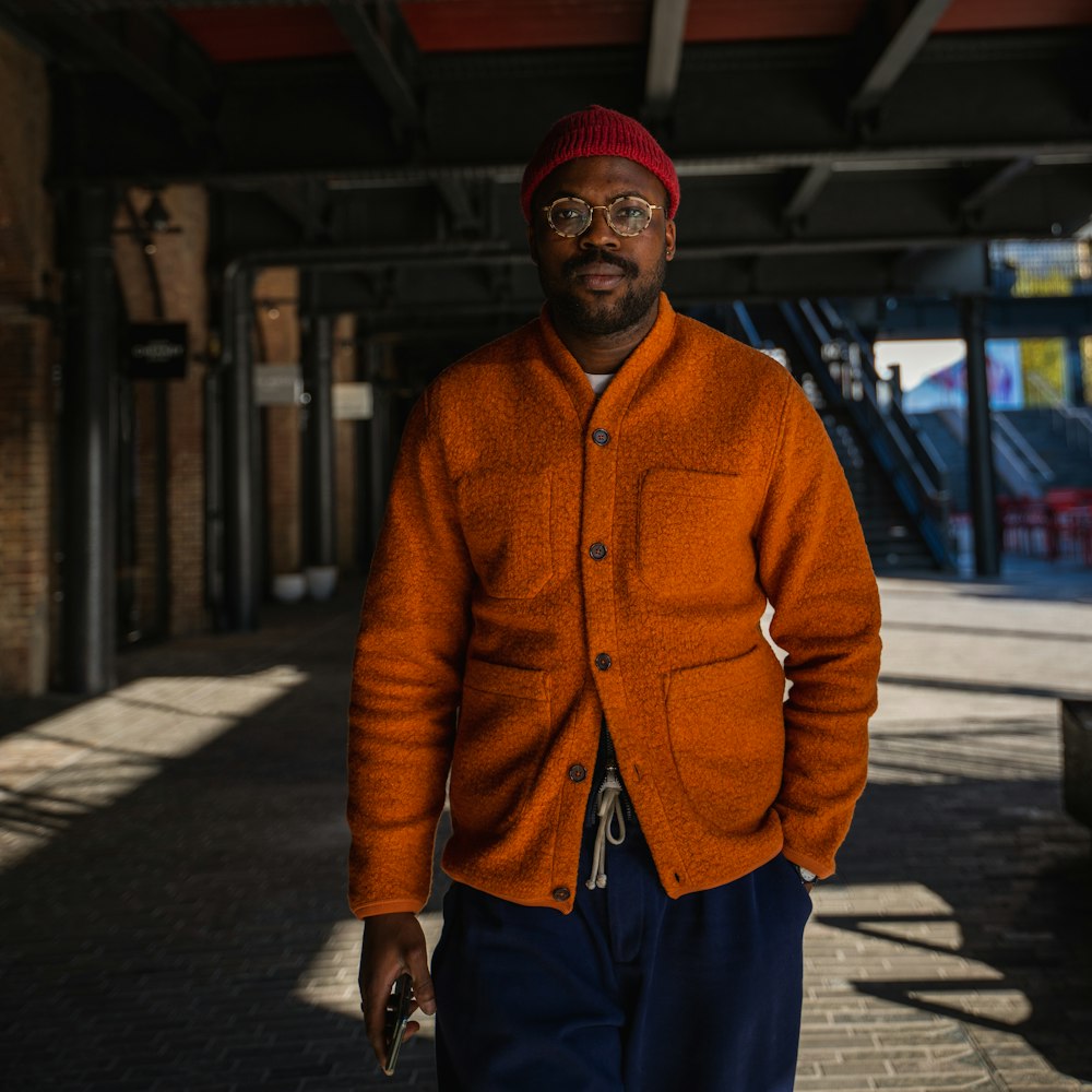 man in orange knit sweater and blue denim jeans standing on sidewalk during daytime