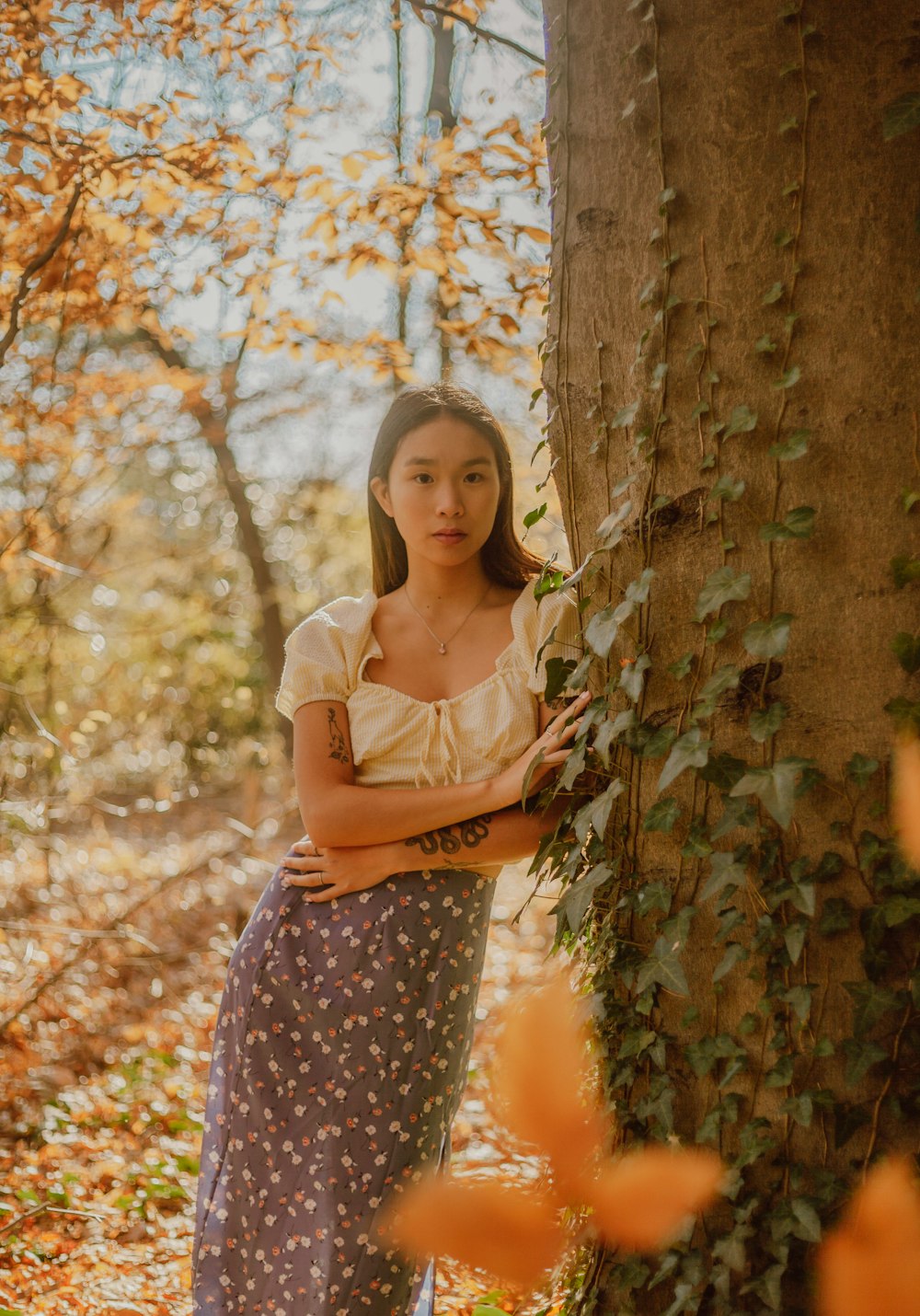 woman in white shirt and purple and white polka dot skirt standing beside brown tree during