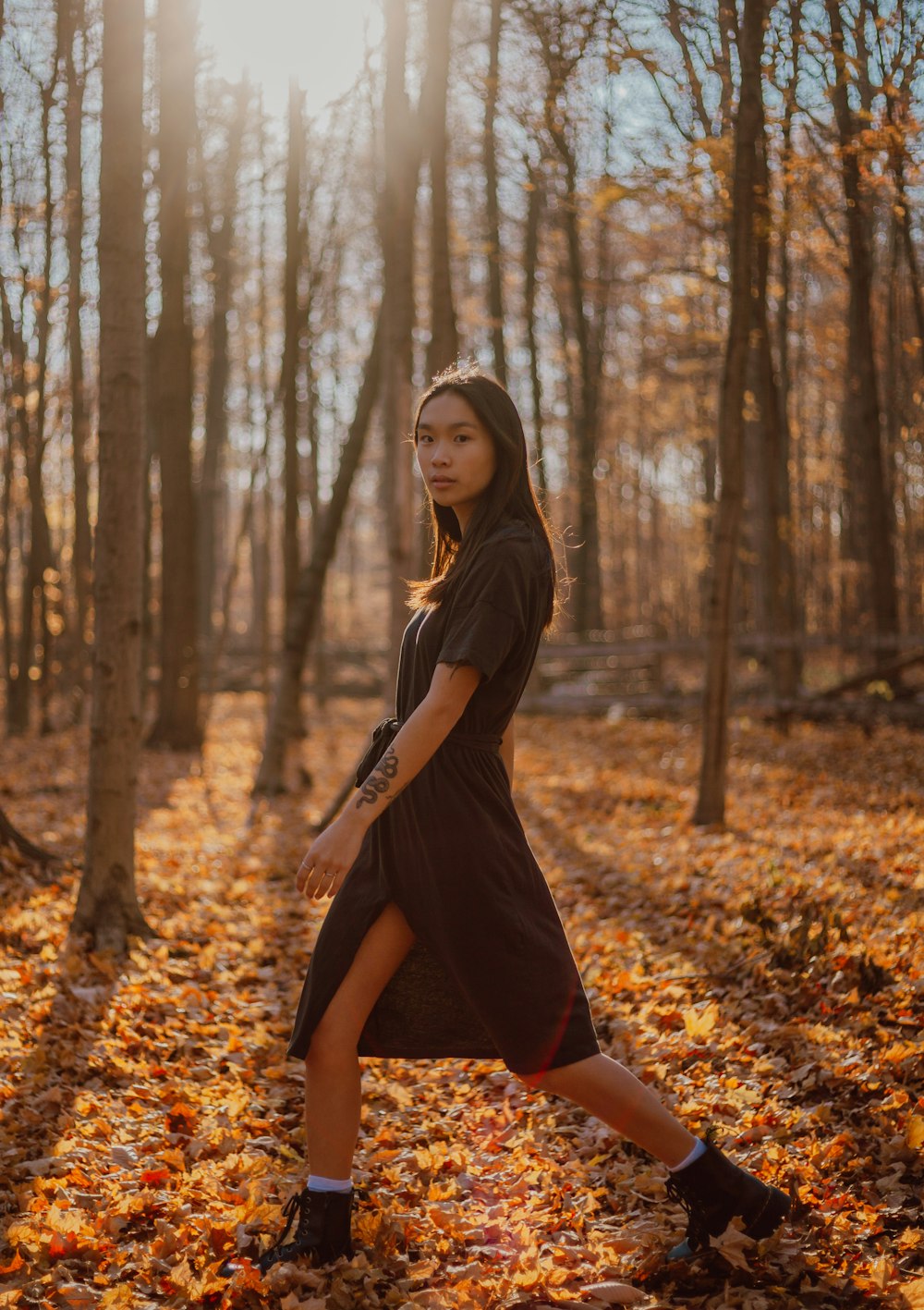woman in black dress standing on brown leaves on forest during daytime