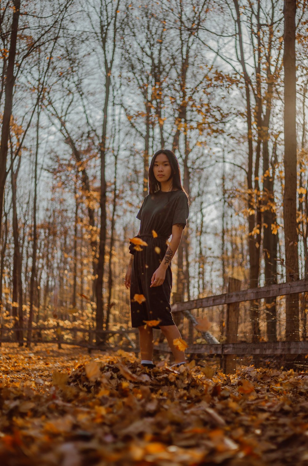 woman in black dress standing on brown dried leaves during daytime