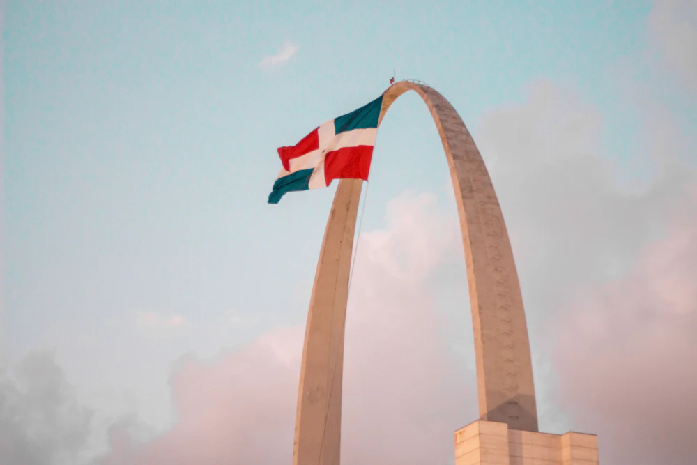 La bandera dominicana ondeando sobre el monumento de la Plaza de la Bandera en Santo Domingo al atardecer