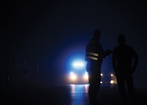 Tow truck driver assisting a stranded motorist on a dark highway with electric blue safety vest.