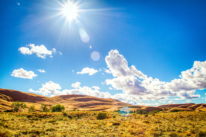 Low sun in a bright blue sky over rolling golden hills and desert scrub