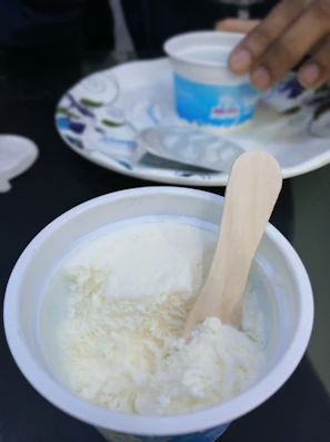 Close-up of a wooden surf-shaped spoon resting on a scoop of melting ice cream under sunlight