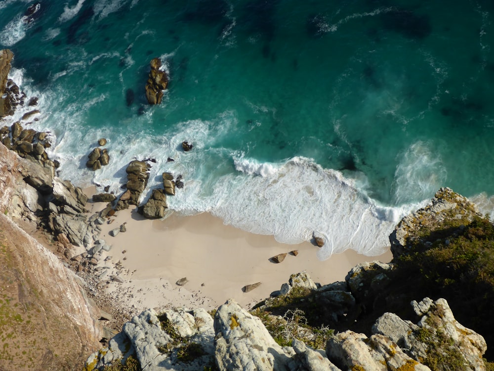 aerial view of sea waves crashing on brown rocky shore during daytime