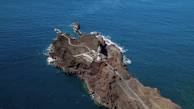 people on top of brown rock formation near body of water during daytime