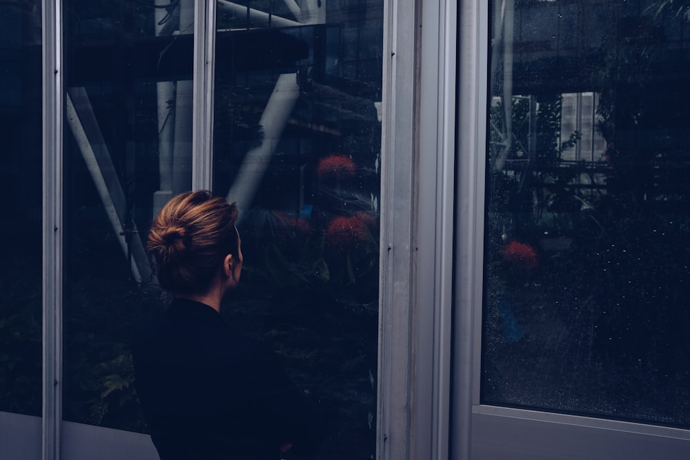 Femme en chemise noire à manches longues debout à côté d’une fenêtre en verre
