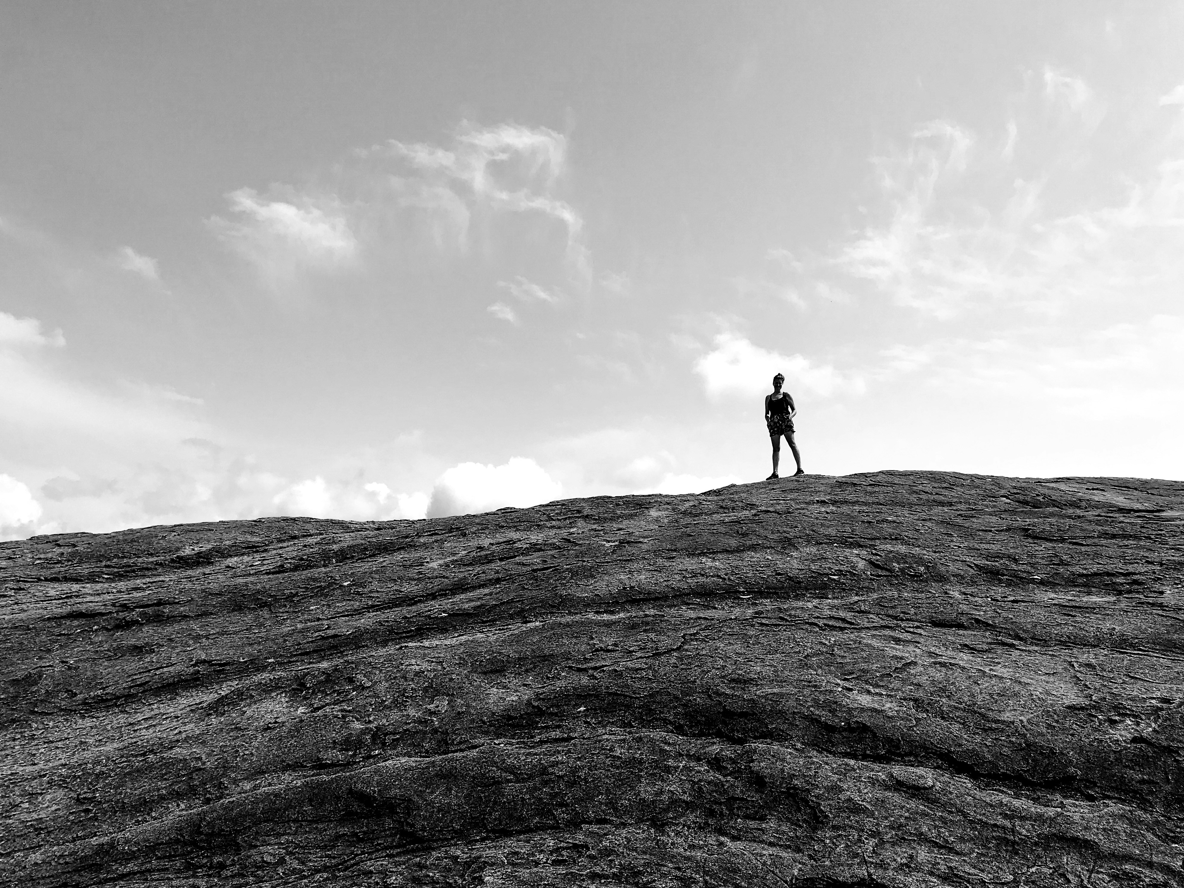 grayscale photo of person standing on rock formation