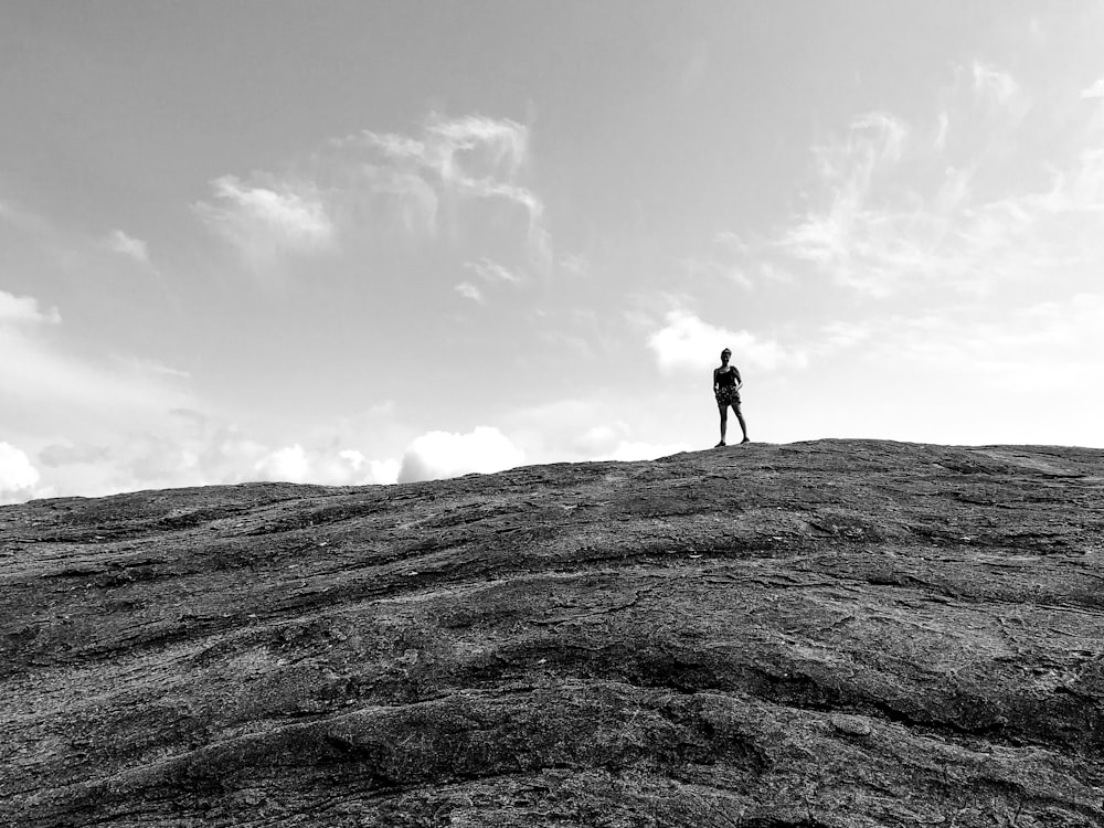 grayscale photo of person standing on rock formation