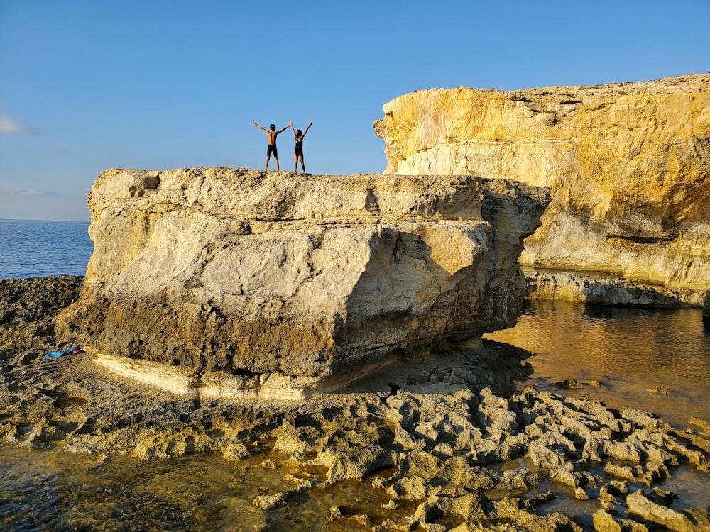 Persona in piedi sulla formazione rocciosa vicino allo specchio d'acqua durante il giorno