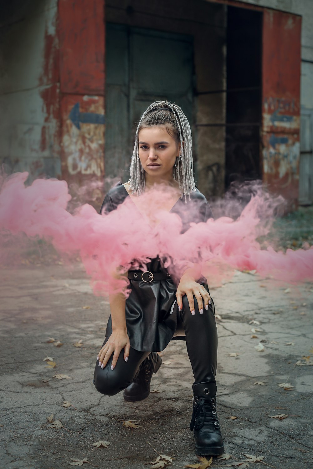 woman in black long sleeve shirt and black pants sitting on concrete floor with pink smoke