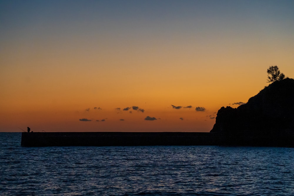 silhouette of rock formation on sea during sunset