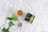 A cup filled with amber-colored tea sits on a light marbled surface. Next to it, there is a green and black box labeled Elixir Slim Amazonite High Quality CBD. A blurred green plant is in the foreground, and a small clear bag with a logo is nearby.