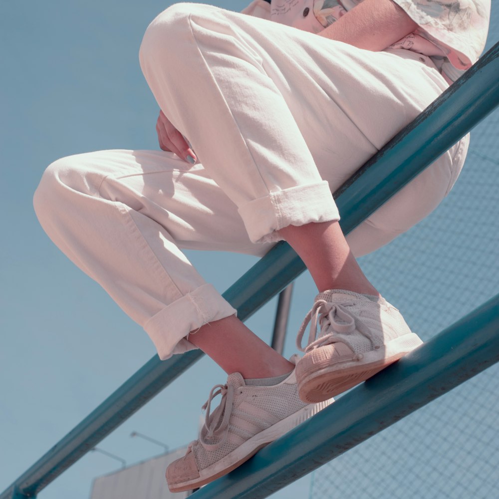 person in white pants and white sneakers sitting on blue metal railings