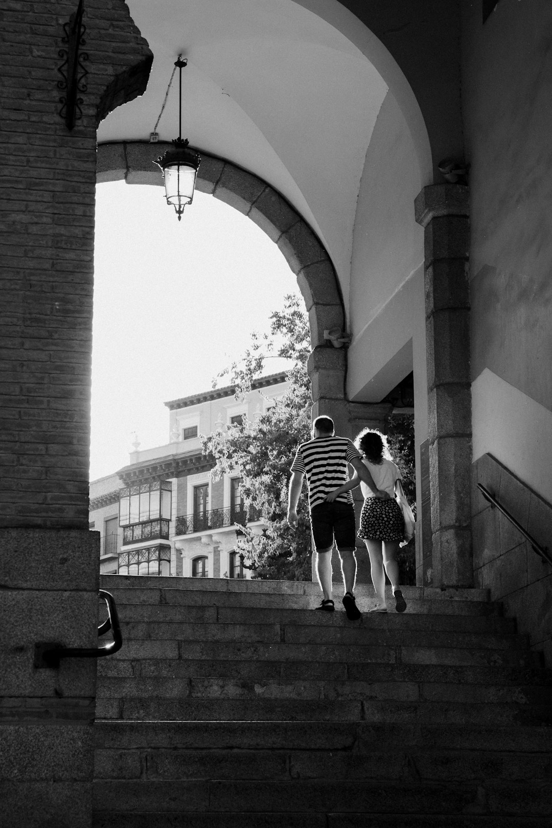 grayscale photo of man and woman walking on sidewalk