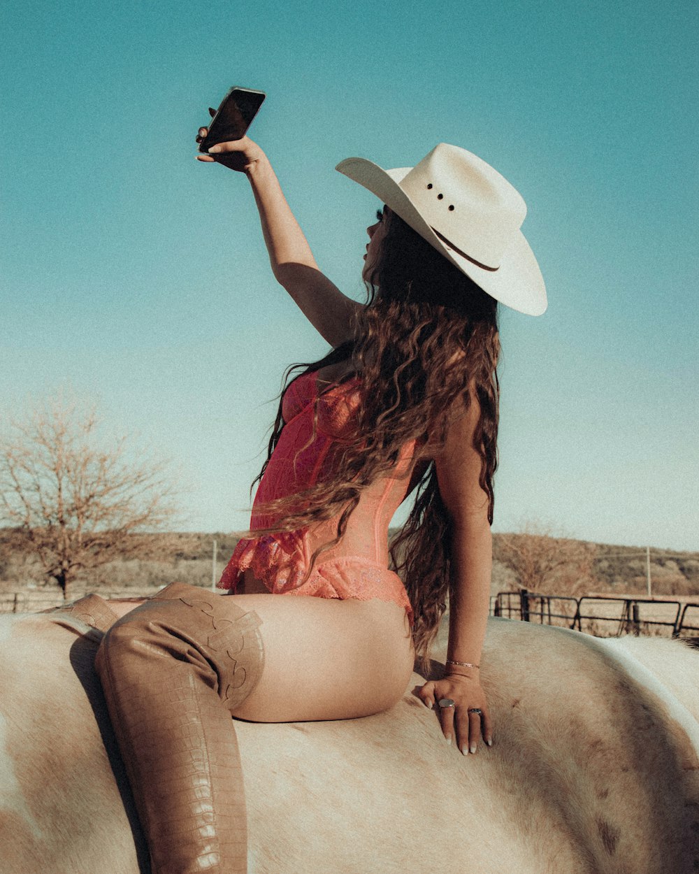 woman in red and black floral sleeveless dress wearing white cowboy hat sitting on brown concrete