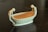 An elegant ceramic dish or bowl, shaped like a boat, adorned with two sculpted figures standing at either end. The figures are gracefully posed and appear to be female, each bowing slightly towards the center. The overall texture is smooth, and the finish is a creamy off-white color.