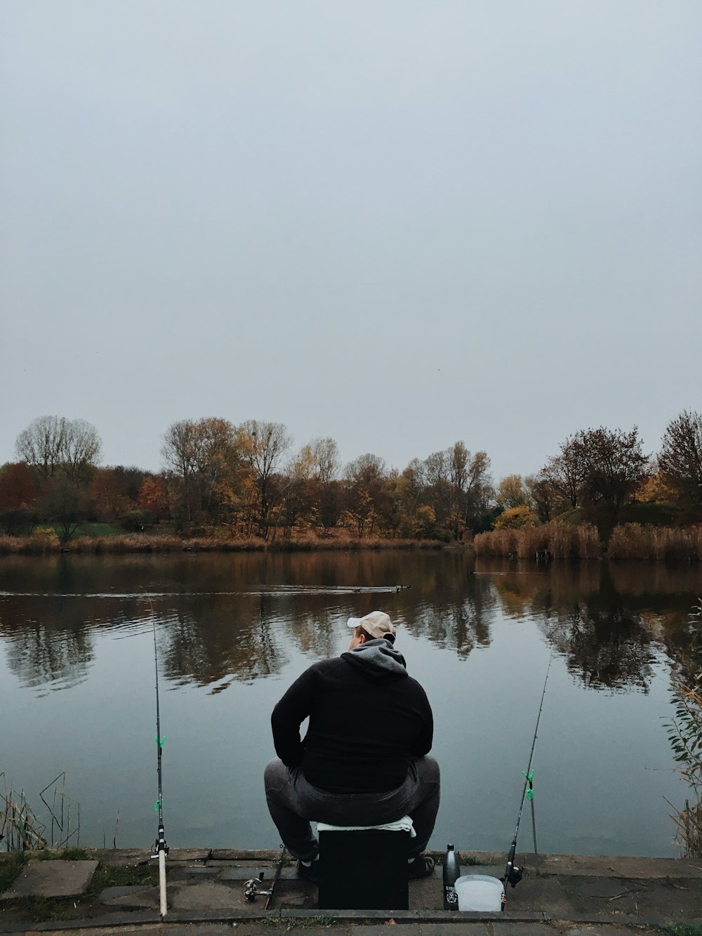 person in black jacket and black pants sitting on rock near lake during daytime