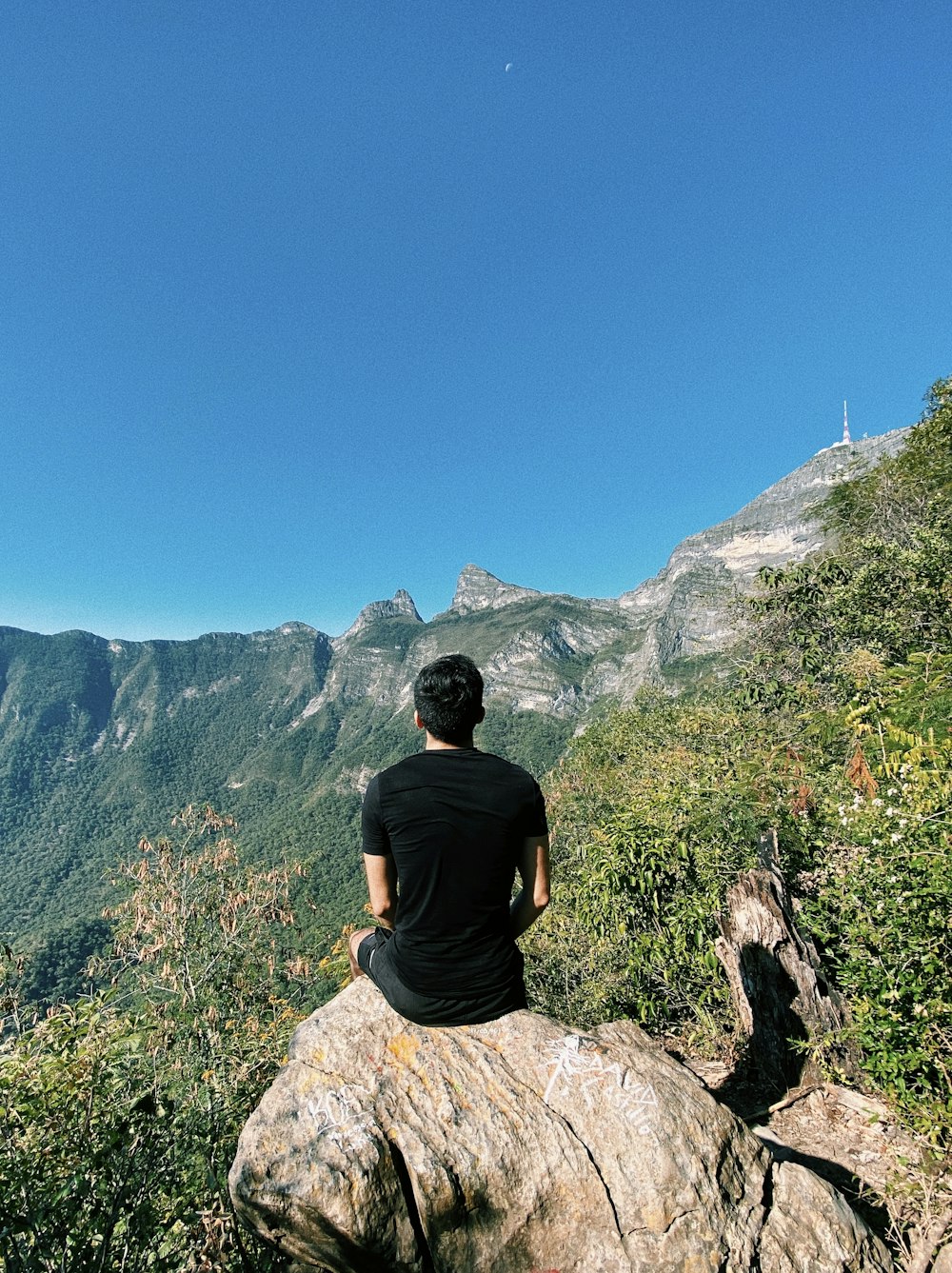 man in black crew neck t-shirt sitting on rock during daytime