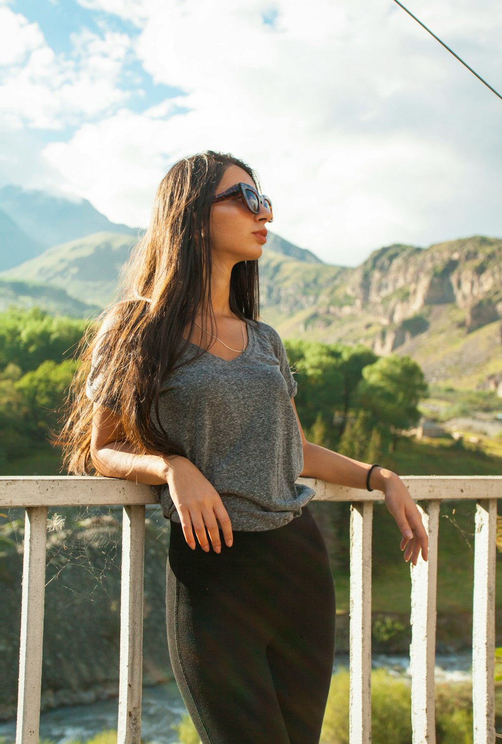 woman in gray crew neck shirt and black pants wearing black sunglasses standing on brown wooden