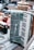 A vintage accordion with a pearl-like finish and black and white keys is prominently displayed on a textured surface. Surrounding it are various other items, including a brass samovar and what appears to be an old radio. The setting suggests a flea market or antique sale atmosphere.