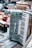 A vintage accordion with a pearl-like finish and black and white keys is prominently displayed on a textured surface. Surrounding it are various other items, including a brass samovar and what appears to be an old radio. The setting suggests a flea market or antique sale atmosphere.
