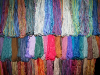 Multiple bundles of colorful yarn hanging in rows, showcasing a wide variety of shades and textures. Each bundle consists of tightly arranged threads, creating a vibrant display.