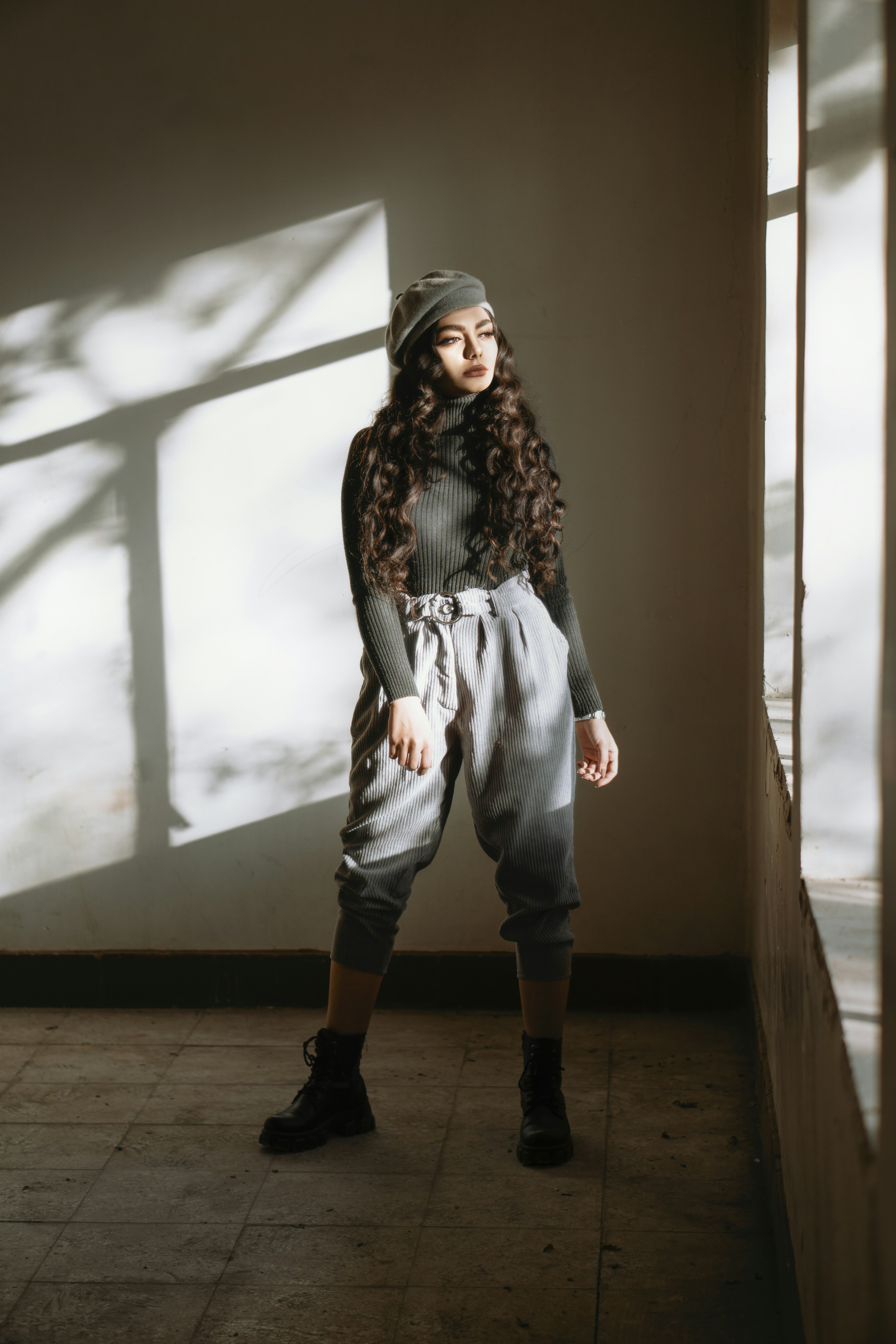 woman-in-black-and-white-coat-and-gray-pants-standing-beside-white-window-curtain