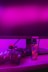 A gaming setup is featured with a camo-patterned game controller and a colorful vaporizer placed on a wooden desk. The background is illuminated with vibrant pink lighting, and a computer monitor with an ASUS logo is visible.