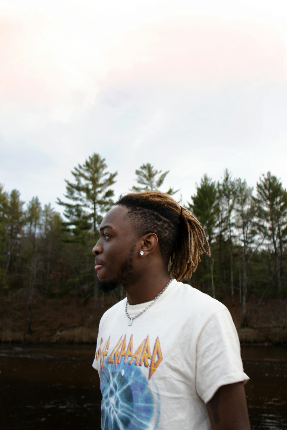 man in white crew neck t-shirt standing near green trees during daytime