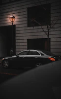 A sleek black vintage car parked under moody streetlights, reflecting the noir aesthetic of the masked nomads.
