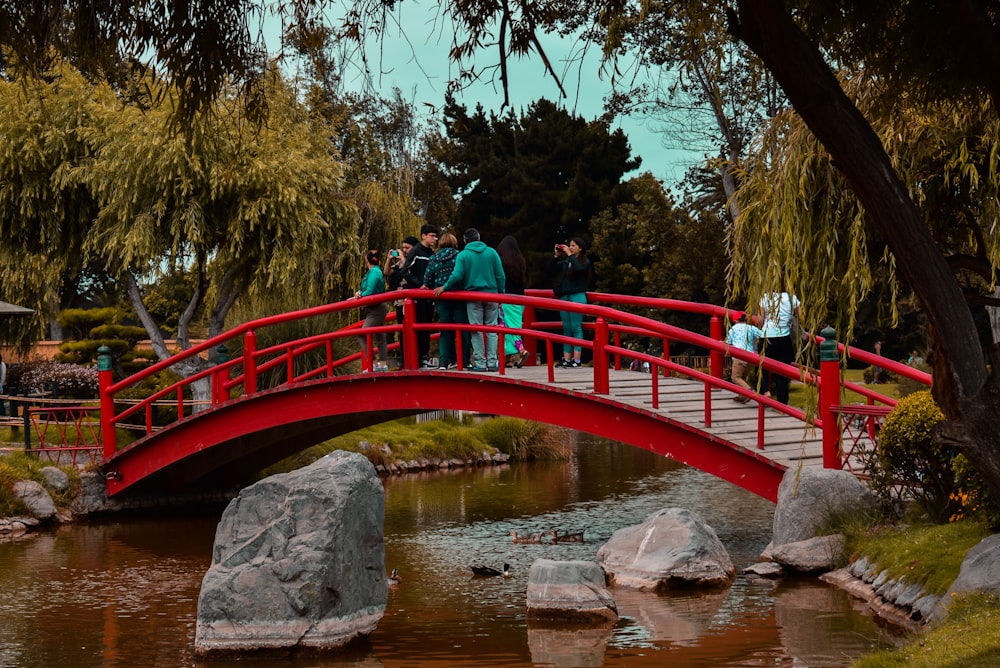 a group of people standing on a red bridge over a pond