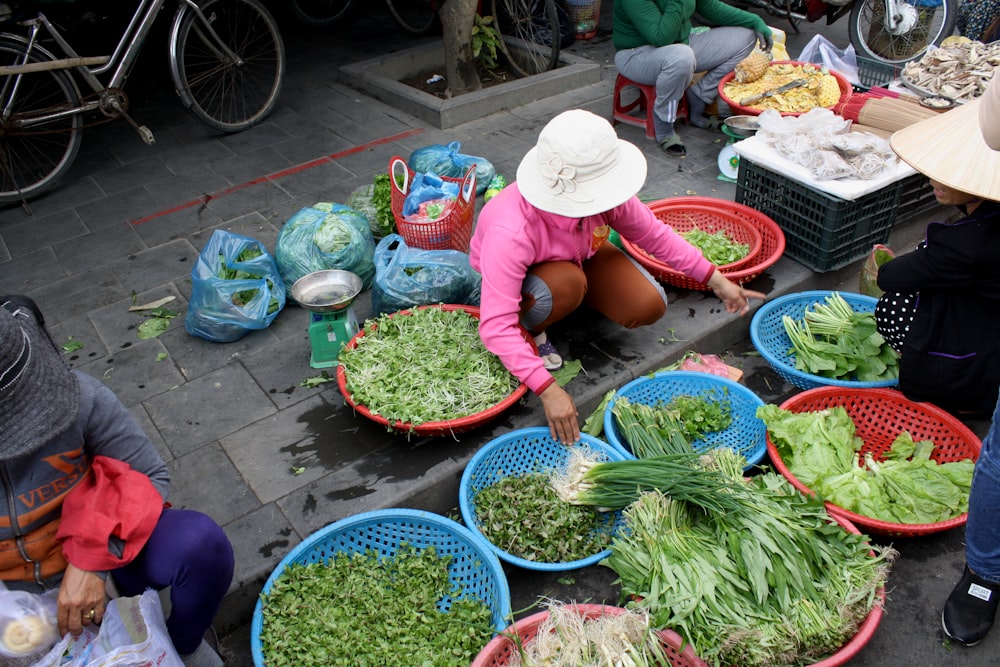 woman in red t-shirt and white hat sitting on the floor with vegetables