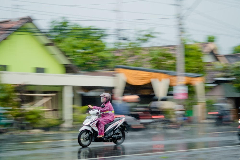 a woman riding a motorcycle down a rain soaked street