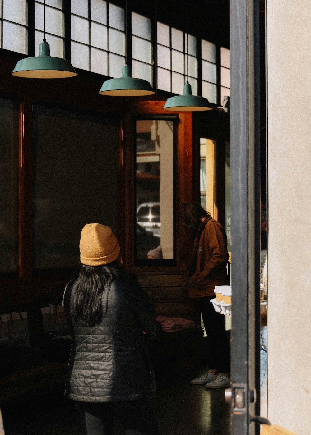 Frau in grauer Jacke und braunem Hut in der Nähe einer braunen Glastür mit Holzrahmen