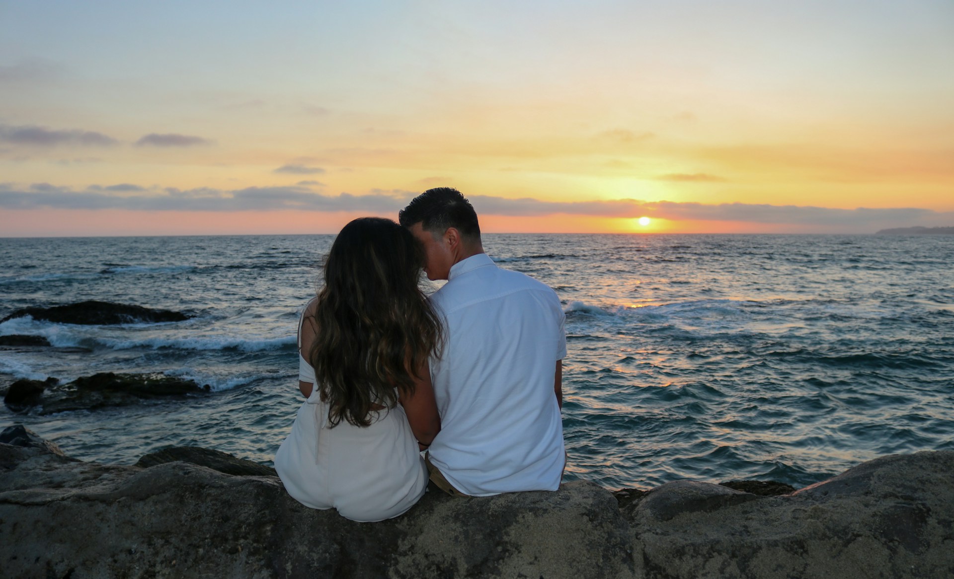 a man and a woman sitting on a rock near the ocean