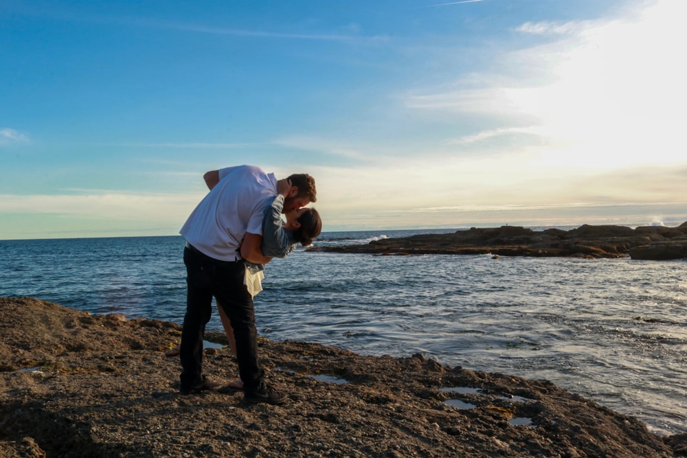 man in blue dress shirt and black pants standing on brown field near body of water