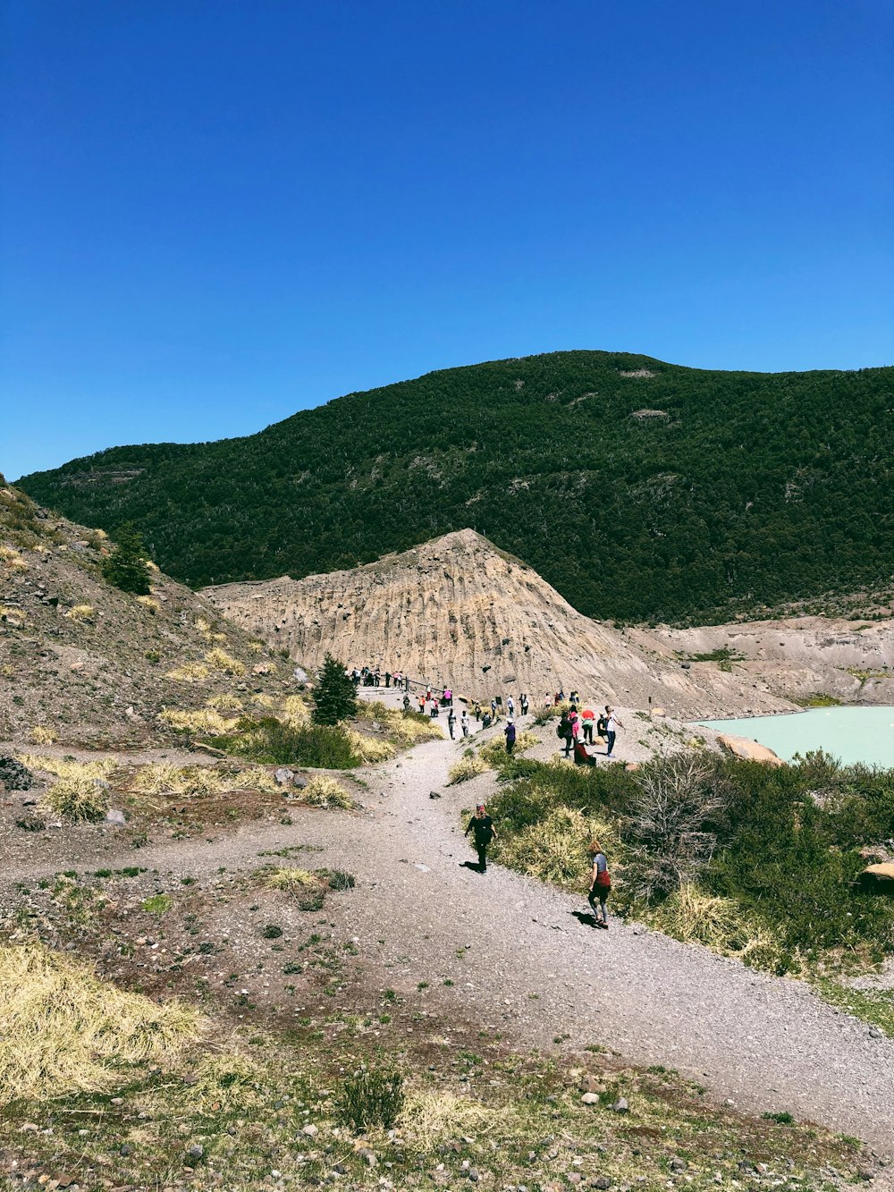 people walking on dirt road near green mountain under blue sky during daytime