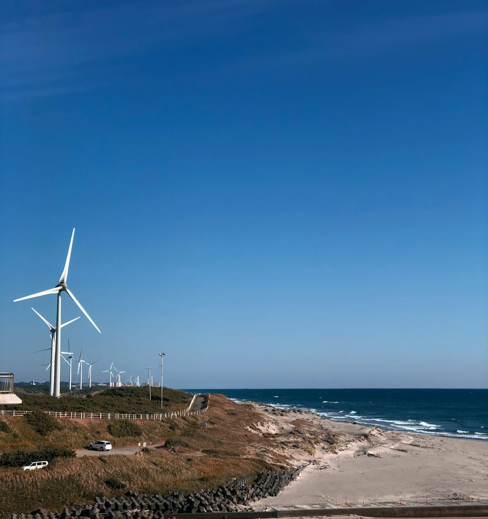 white wind turbines on brown field near body of water during daytime