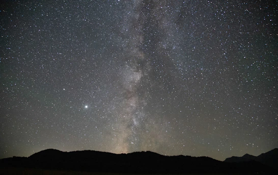 An awe-inspiring view of the Milky Way stretching across a dark night sky above a quiet mountain landscape.