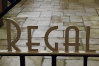 Metallic letters spelling 'REGAL' are mounted on a gate, with a stone-paved walkway visible in the background.