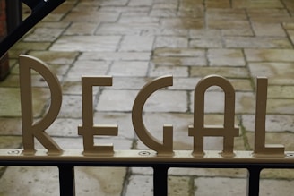 Metallic letters spelling 'REGAL' are mounted on a gate, with a stone-paved walkway visible in the background.