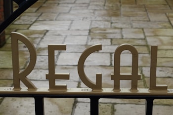 Metallic letters spelling 'REGAL' are mounted on a gate, with a stone-paved walkway visible in the background.
