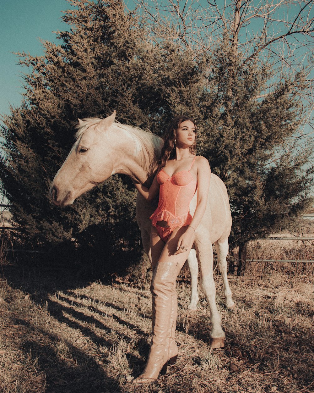 woman in pink long sleeve shirt and white pants standing beside white horse during daytime
