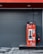 A vibrant red coffee vending machine is stationed against a dark gray, paneled wall. The machine is adorned with white ornamental swirls and text in another language. A large cable extends from the top of the machine. To the right of the vending machine is a red, cylindrical trash can with a black stand.