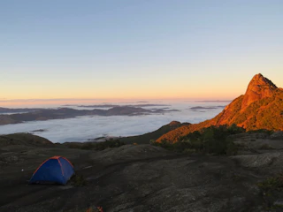 A rugged mountain landscape at dawn with a lone adventurer standing beside a geodesic dome tent.